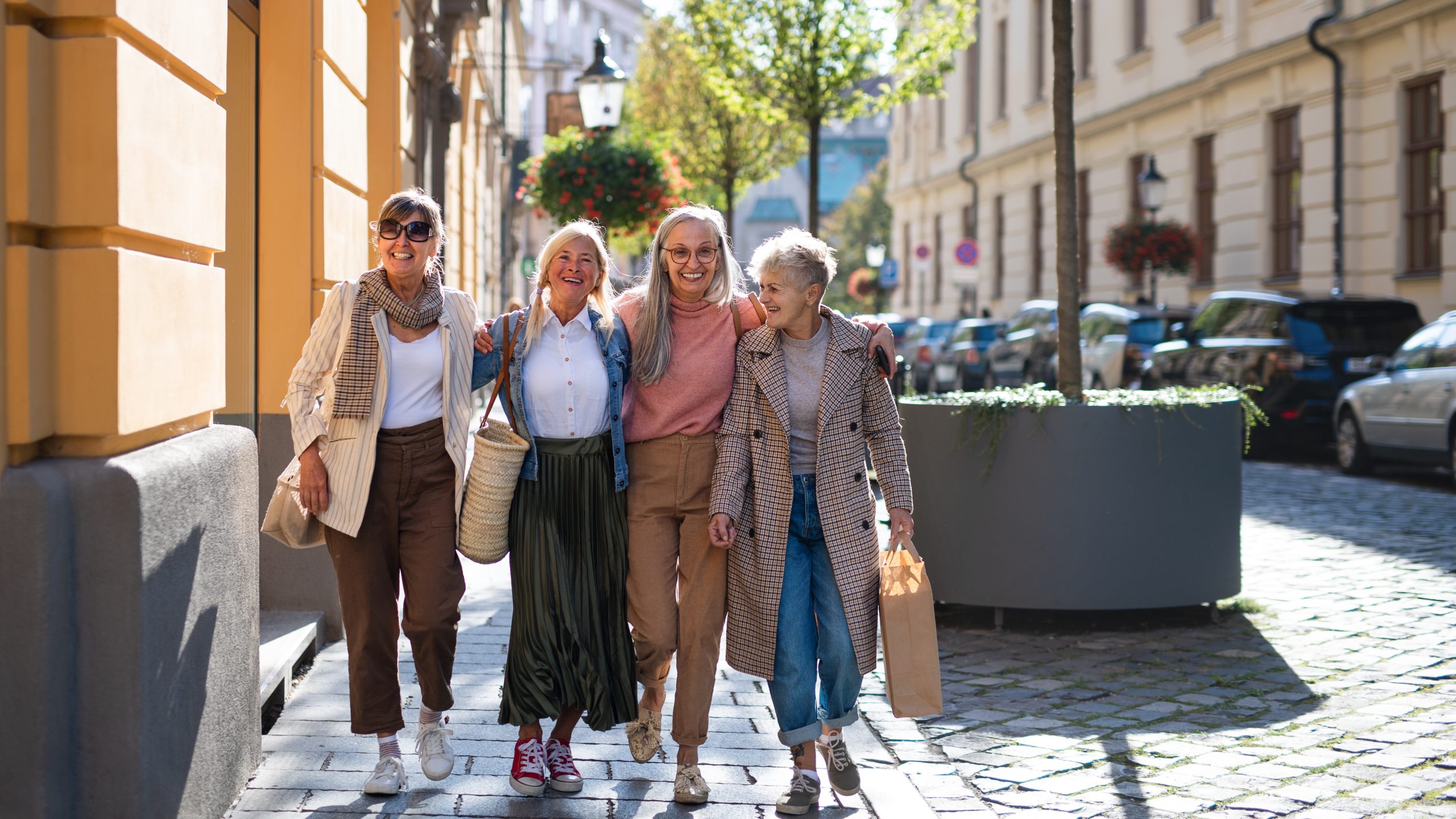 Group of happy senior women walking and holding outdoors in town, looking at camera.
