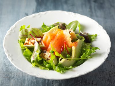 Salaattilautanen pöydällä. Salaatissa mm. lohta graavilojta, juustoleipää, avocadoa ja salaattia.