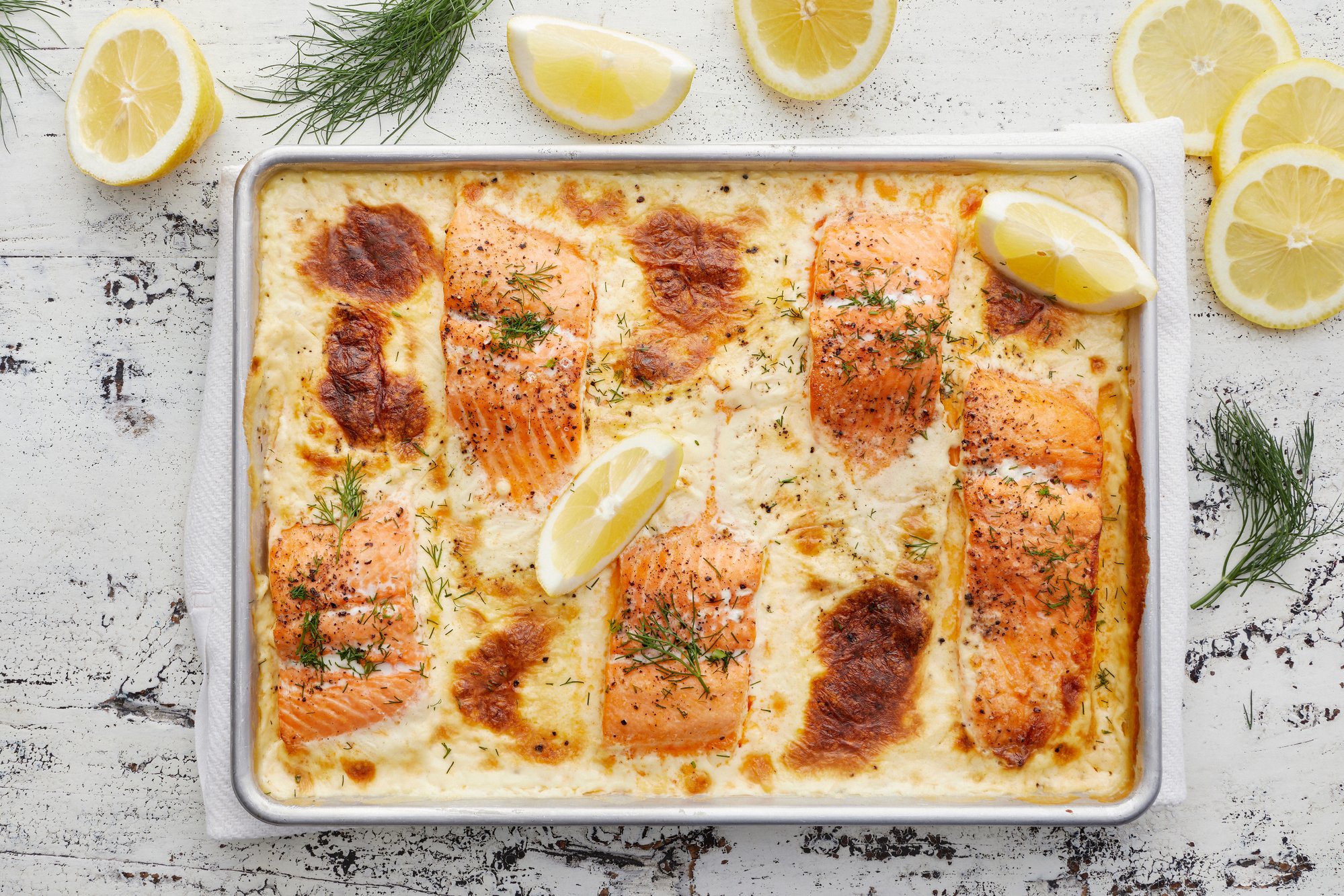 Ylhäältä kuvattu kokonainen uunilohivuoka. Kuvassa myös sitruunalohkoja ja tilliä.