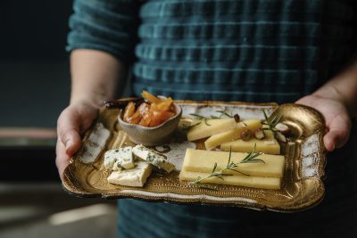 Juustoja kultaisella tarjottimella, jota ihminen pitää käsissään