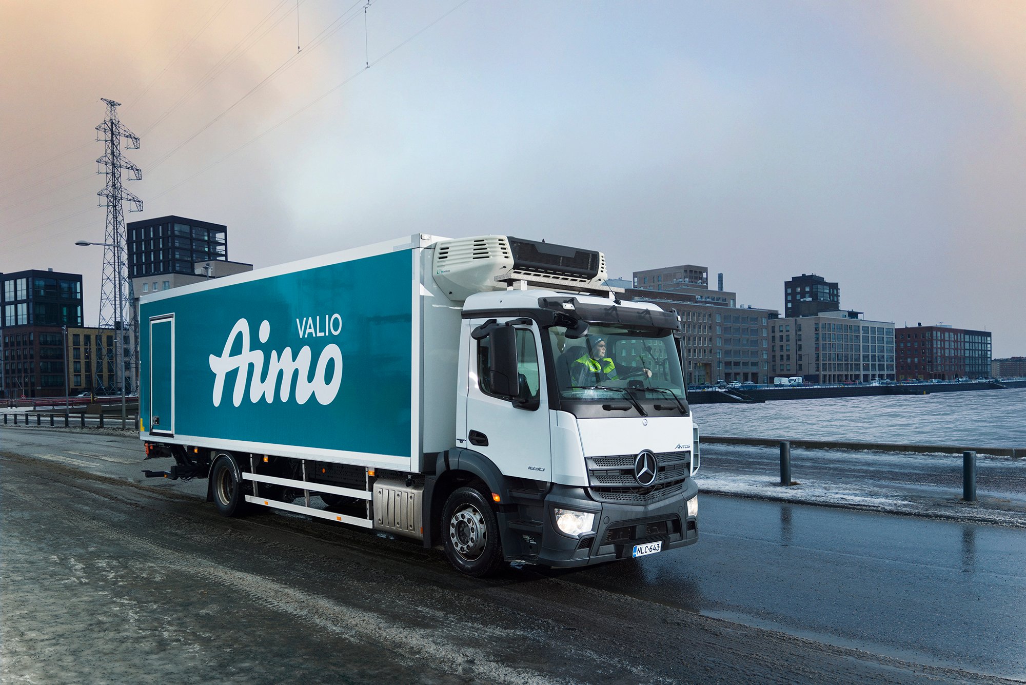 Kuvassa talvisessa Helsingin maisemassa on Valio Aimo rekka-auto kuvattuna sivuttain ajamassa eteenpäin tiellä.