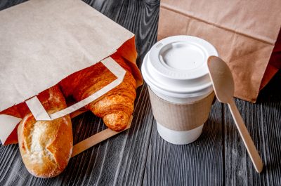 Take away välipalaa pöydällä - croissantteja pussissa ja kahvia mukissa.