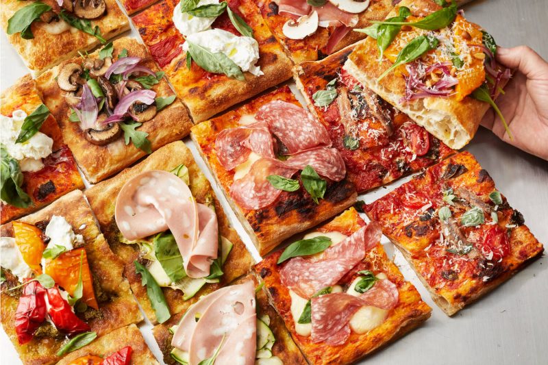 Pizza al taglio, roomalaisen levypizzan paloja erilaisin täyttein ja yhdessä kädessä on palapizzaa.