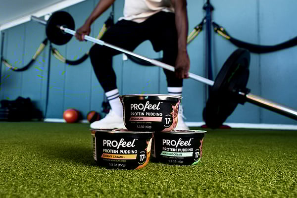 Man lifting weights with PROfeel protein pudding in the foreground